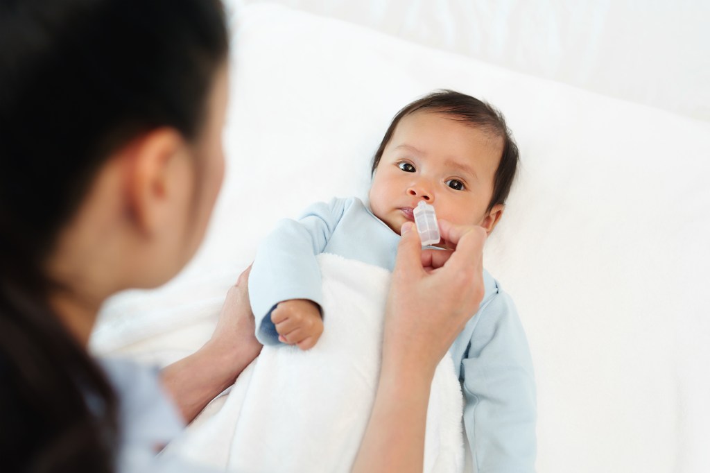 The newborn baby receives nasal drops from the mother in bed