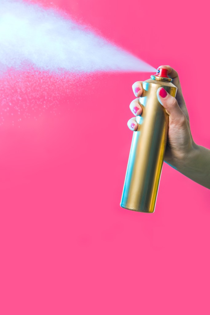 Woman's hand spraying hairspray on a red background